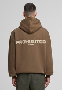 Brun hættebluse med stor, cremefarvet "FORBUDT" tekst og "10119, BERLIN" på ryggen. Har snor i hætten og ribbede manchetter.