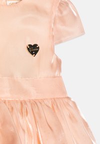 Robe en satin rose avec des manches courtes bouffantes, une jupe froncée et un logo en forme de cœur noir avec des accents dorés sur la poitrine.
