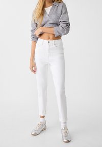 White high-waisted jeans with a slim fit, paired with a gray cropped sweater and silver sneakers, showcasing a casual style.