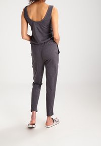 Top gris sin mangas con escote en la espalda, combinado con pantalones ajustados a juego, que presentan una cinturilla elástica y bolsillos laterales, usados con sandalias tipo destalonadas.
