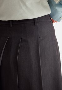 Pantaloni plissettati grigio scuro con una texture liscia e cintura, caratterizzati da dettagli di cucitura discreti e un design su misura.