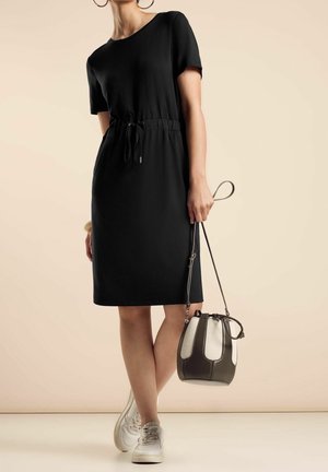 Zwarte jurk met korte mouwen en een elastische taille. Gecombineerd met witte sneakers en een bucketbag in twee tinten, met donkere en lichte gedeeltes.