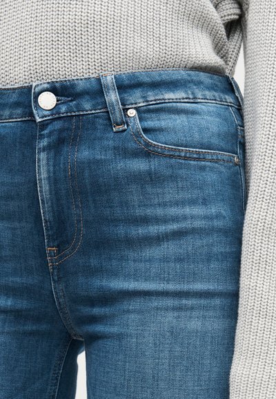 Jeans i mellanfärgad blå denim med en jämn textur, med kopparfärgad söm, en silverknapp och en standarddesign med fem fickor.