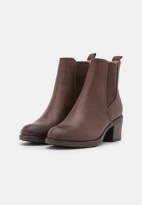Bottes de cheville en cuir marron avec une finition texturée, panneaux latéraux élastiques et un petit talon empilé. Équipées de languettes pour un enfilage facile.