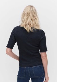 Svart, texturerad topp med korta ärmar, figurnära passform och lätt fransad nederkant. I kombination med blå denimjeans. Inga synliga mönster eller detaljer.