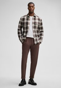 Gekleurde blouse in beige en bruine tinten met knoopsluiting, gecombineerd met bruine tapered broek en zwarte veterschoenen. Eenvoudig, schoon ontwerp.