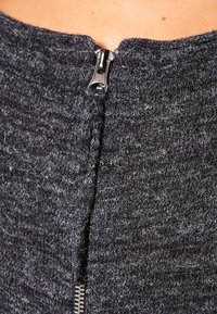 Top de punto gris con un cuello alto, que presenta una cremallera plateada y una textura suave. Tiene un diseño ajustado.
