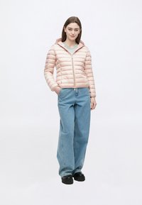 Lyserød pufferjakke med hætte, lynlåslukning foran og quiltet design. Kombineret med løstsiddende blå denimjeans og sorte sko.