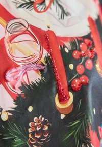 Roter Stoff mit Feiertagsmotiven, darunter ein Glas, Kerzen und Ornamente. Strukturelle Akzente mit Perlenstickerei und einem Detail in Form einer Tannenzapfen.