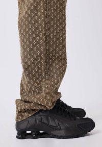 Pantaloni brown con una texture a rilievo a motivo floreale abbinati a scarpe Nike Shox nere, con un design distintivo della suola a molla.