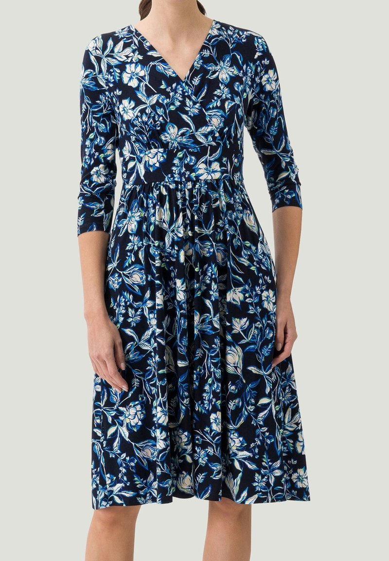 Vestido envolvente floral en azul marino con patrones florales en blanco y azul. Presenta mangas de tres cuartos y una cintura fruncida para una silueta fluida.