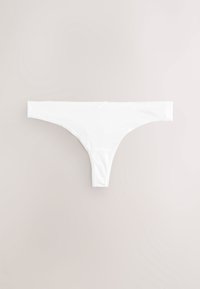 String blanc sans coutures posé à plat sur un fond beige clair avec un petit nœud centré à la taille.