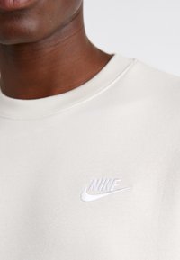 Light beige sweatshirt made from soft fabric, featuring a round neck and a white embroidered Nike logo on the chest.