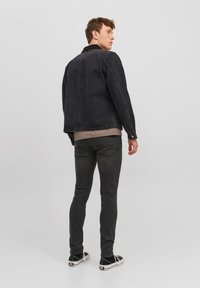 Jachetă din denim negru cu guler, mâneci lungi și croială dreptă, asociată cu blugi închiși la culoare și adidași negri.