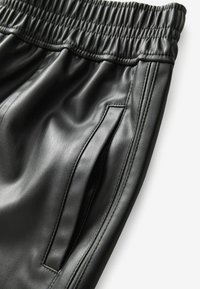 Pantalons en cuir synthétique noir avec une taille élastique, présentant des poches latérales et des détails cousus le long des coutures. Texture douce et lisse.