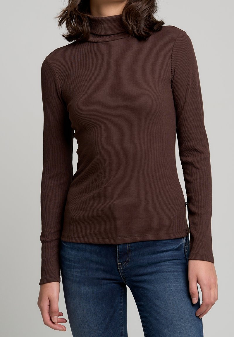 Haut à col roulé long en maille côtelée marron avec un corps ajusté et une texture légèrement extensible, associé à un jean bleu.