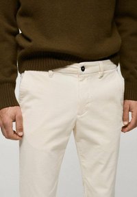Krémové kordové nohavice so slim fit strihom, s gombíkovým zapínaním a prednými vreckami. Skombinované s tmavozeleným pleteným sveterom.