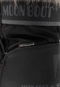 Närbild av svarta Moon Boot med ett vattentätt märke som är sytt nära toppen, med detaljerad sömnad och texturerade syntetmaterial.