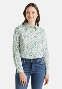 Camicia botton-down in cotone verde chiaro con un motivo floreale blu e verde. Presenta un colletto e maniche lunghe, abbinata a jeans blu.