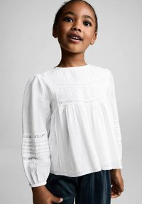 Witte blouse met lange mouwen, met geplooide textuur en kantdetails op de mouwen. Ronde hals en een losse pasvorm. G gedragen met donkere broek.