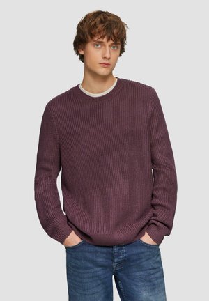 Paarse gebreide trui voor mannen met een gestructureerd patroon, ronde hals en lange mouwen, gecombineerd met blauwe jeans. Effen achtergrond.
