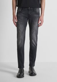 Pantalones vaqueros de mezclilla negra con corte ajustado, lavado deslavado, cinco bolsillos y detalles de botón de metal, combinados con botas negras.