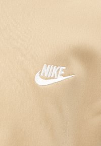 Μπεζ ύφασμα με υφή, με λευκό κεντημένο λογότυπο Nike στην αριστερή πλευρά. Απλός σχεδιασμός, χωρίς επιπλέον σχέδια.