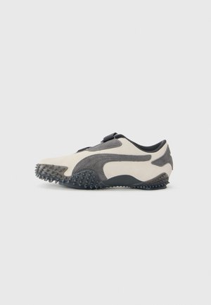 Beige and dark gray athletic shoe with spike-studded sole and strap closure, viewed from the side on a white background.