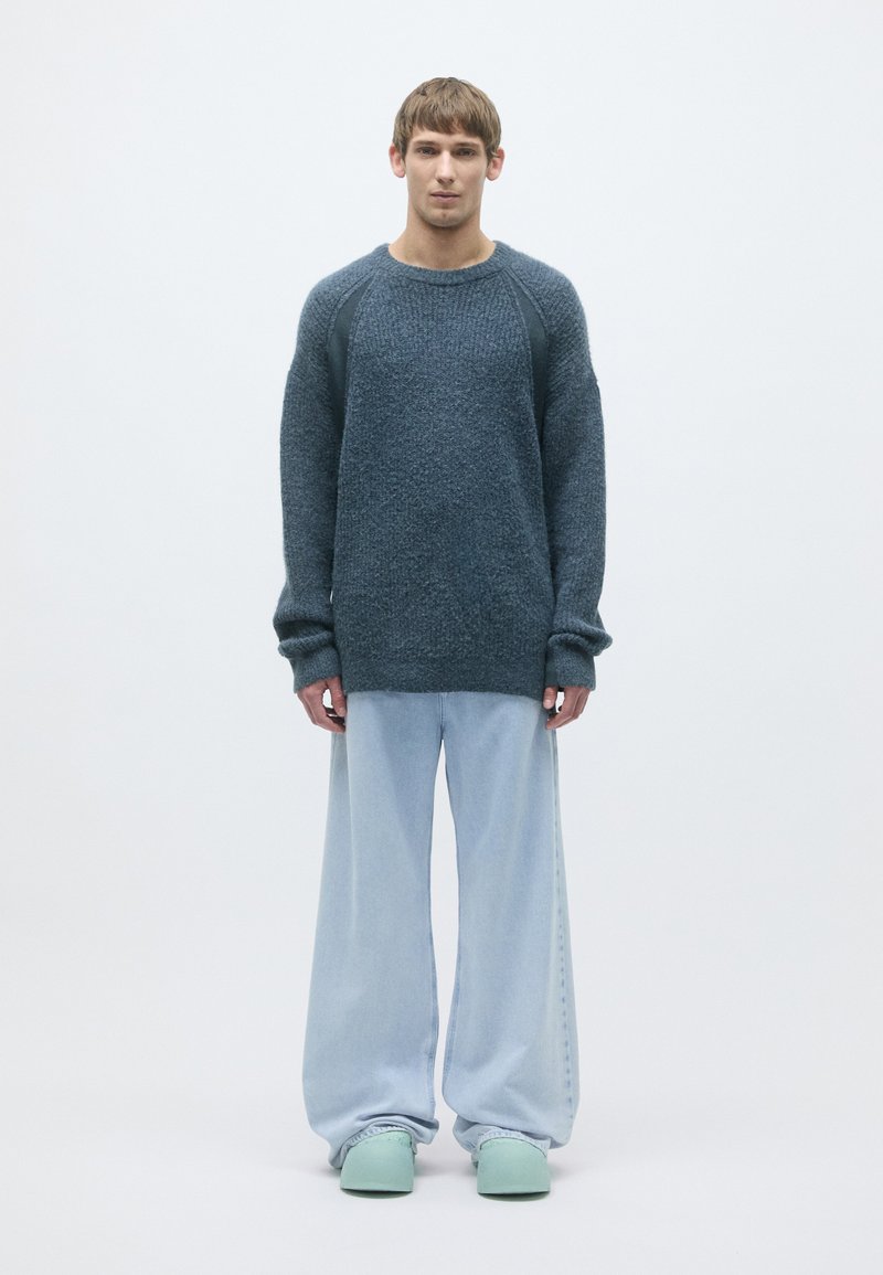 Sötétkék, texturált pulóver, raglan ujjakkal, világoskék, bő szárú farmerral és menta zöld slip-on cipővel párosítva.