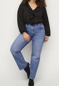 Czarna bluzka z falbanami przy dekolcie, w połączeniu z niebieskimi dżinsami o wysokim stanie i prostych nogawkach. Czarne botki za kostkę dopełniają outfit.