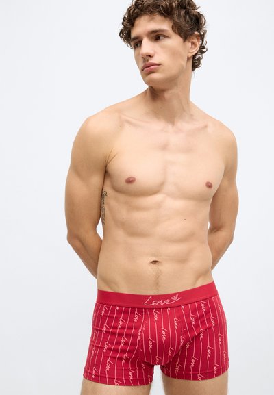 Červené boxerky s vertikálnym bielym vzorom textu „Love“. Elastický pás má zhodný text. Tkanina vyzerá mäkko, pružne a ľahko.