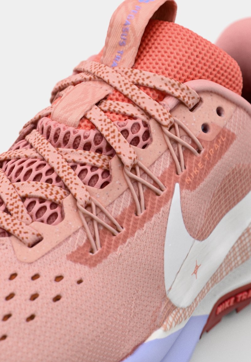 Różowe buty sportowe z teksturowanej siateczki, z wyraźnym białym logo swoosh i skomplikowanym wzorem sznurówek. Lekkie z kontrastującą podeszwą.