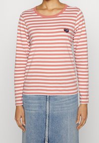 Langärmliges T-Shirt in Koralle und weißen Streifen, Rundhalsausschnitt, mit einem kleinen gestickten Herzdetail auf der Brust. Material aus Baumwollmischung.