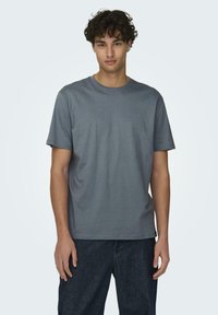 Graues Baumwoll-T-Shirt mit kurzen Ärmeln und Rundhalsausschnitt, mit glatter Textur und geradem Schnitt, kombiniert mit dunkler Jeans.