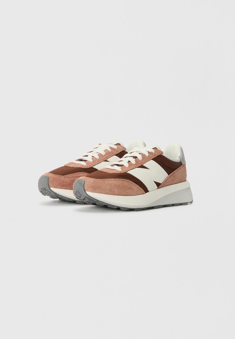 Baskets en suede roses et marron avec un logo blanc, des panneaux texturés et une semelle en caoutchouc grise. Comprend des lacets et une languette rembourrée.