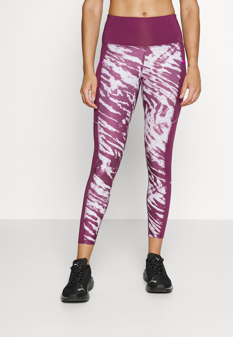 Leggings viola con un motivo a strisce di tigre bianche e una cintura larga, dotati di tasche laterali e un tessuto liscio e elastico.