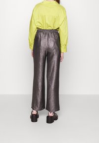 En limegrön skjorta instoppad i glänsande, mörksilverfärgade, vida byxor med elastisk midja, kombinerat med klumpiga svarta platåskor.