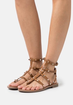 Brune gladiator sandaler med flere stropper og metal pyramide studs. Flad sål og åbent tå-design forbedrer åndbarheden.