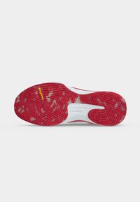 Semelle de chaussure de sport rouge et blanche avec une bande de roulement texturée et un logo Goodyear jaune sur un fond gris clair uni.