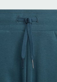 Pohodlné kalhoty z tkaniny v barvě bílé s plochým stahovacím šňůrkou v pase, která je zakončena kovovými koncovkami a provlečena zesílenými dírami.