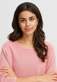 Maglione leggero rosa a maglia con scollo rotondo e maniche lunghe, caratterizzato da un motivo testurizzato. La modella ha capelli lunghi e mossi.