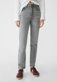 Jeans de talle alto grises de mezclilla, con un diseño de pierna recta, un ligero desgastado y un cierre de botones clásico. Combinados con zapatillas oscuras.
