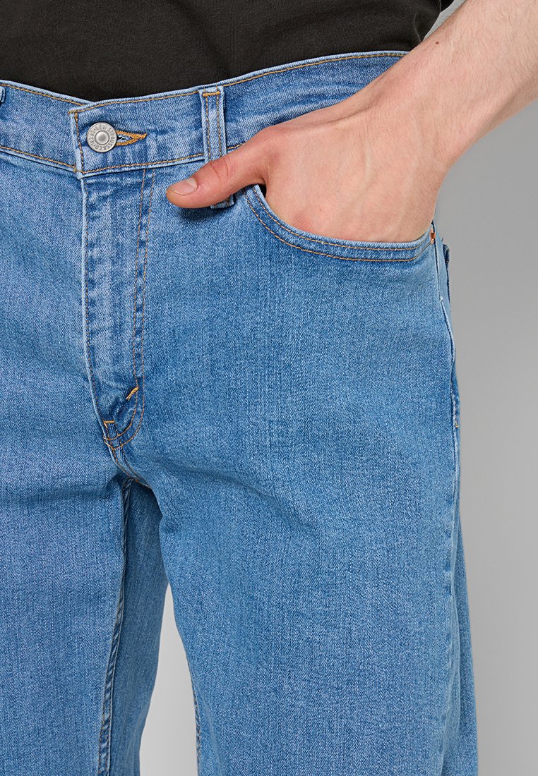 Jean en denim bleu clair avec une coupe droite, présentant une poche visible, des coutures orange contrastantes et une fermeture à bouton en métal.