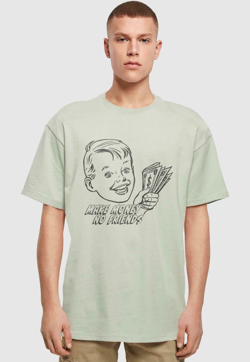 Svetle zelené oversized tričko s grafikou usmívajícího se chlapce, který drží peníze, a textem "VYDĚLEJ PENÍZE, NE PŘÁTELE" v tučných písmenech.