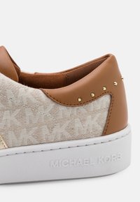 Sneaker in pelle marrone chiaro e tessuto con motivo, decorata con borchie dorate e suola bianca, con logo "MICHAEL KORS" in rilievo sul tallone.