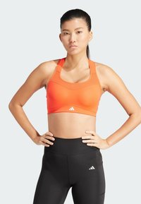Oranje sportbeha met een ronde hals, dikke banden en logodetail. Gecombineerd met hoge zwarte legging met een soortgelijk logo.