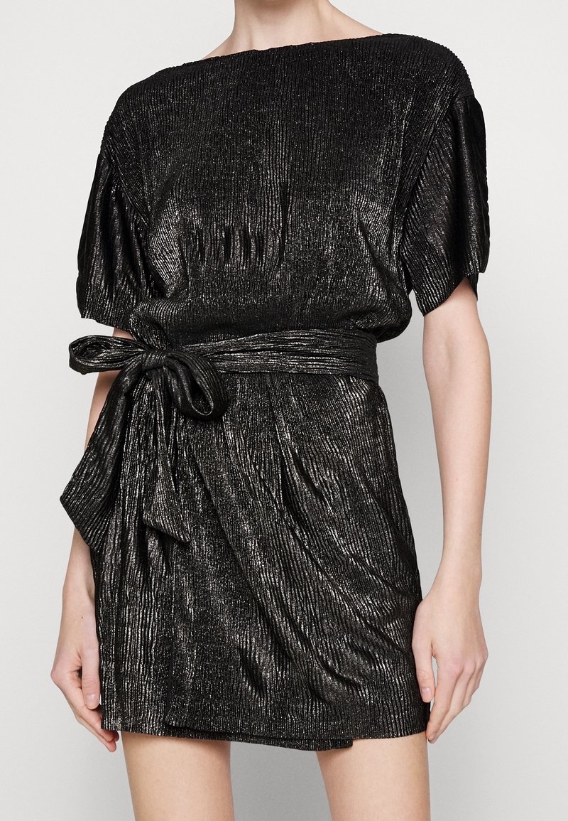 Robe plissée noire et métallique avec de courtes manches bouffantes, un col large et une ceinture nouée à la taille, créant une silhouette structurée et drapée.