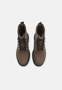 Stivaletti in pelle marrone con lacci neri, occhielli in argento e superficie testurizzata. Presentano una linguetta e una suola nera a contrasto.