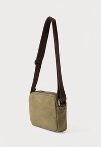 Τσάντα ώμου από καμβά σε ελιά πράσινη με καφέ ρυθμιζόμενο λουρί, ορθογώνιο σχήμα, κλείσιμο με φερμουάρ και λεία υφή.