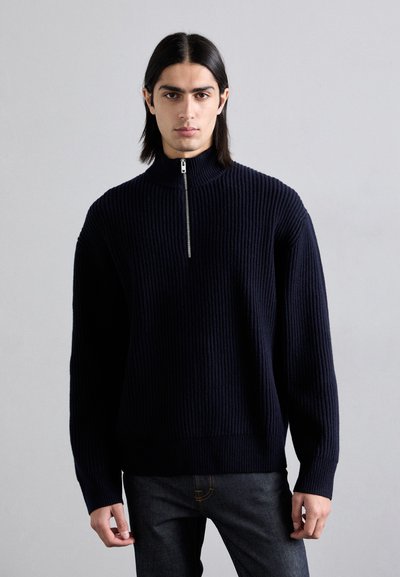 Pull en maille côtelée bleu marine avec un col haut et une fermeture éclair à mi-hauteur. Il possède des manches longues et une coupe décontractée, fabriqué en tissu tricoté texturé.